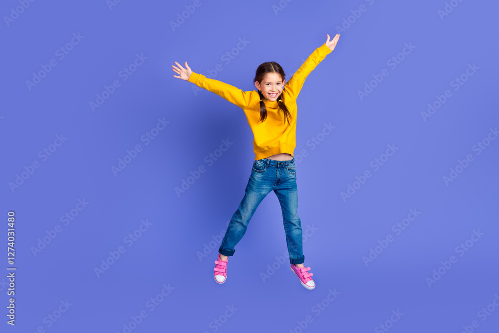 Cheerful young girl jumping with open arms wearing casual yellow sweatshirt against a purple background Cheerful young girl jumping with open arms wearing casual yellow sweatshirt against a purple background