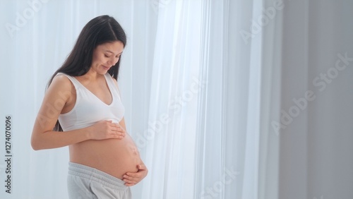 Young happy Asian pregnant woman posing in studio with white curtains in background Free Download Young happy Asian pregnant woman posing in studio with white curtains in background - GFXLoad
