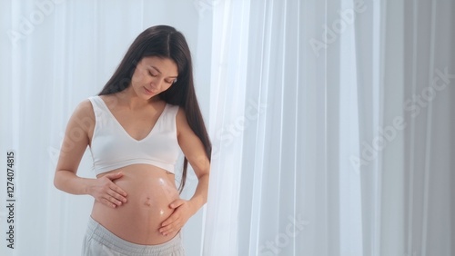 Young happy Asian pregnant woman posing in studio with white curtains in background Free Download Young happy Asian pregnant woman posing in studio with white curtains in background - GFXLoad