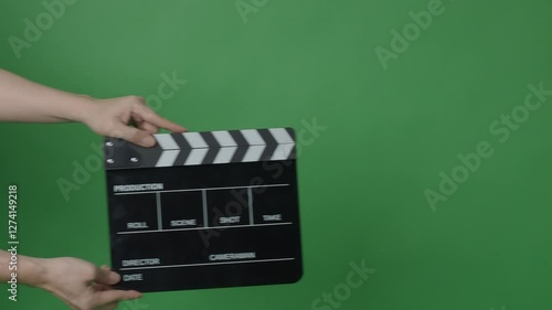 A classic black and white film clapperboard or movie slate being held in front of a green screen. Essential filmmaking tool is used to mark scenes and synchronize audio and video in film production.