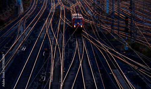 A single electric locomotive makes its way through the complicated track network of a freight yard in Hagen (NRW, Germany) in the twilight of the rising sun. Railroad panorama with glistening tracks.