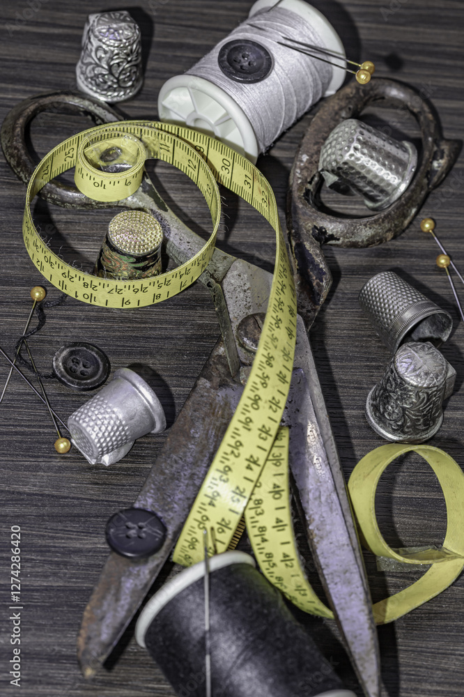 Silver sewing needles, Thimbles, Steel scissors, Measuring tape, Black buttons, Spools of black and white thread including pins on wooden blackground. Sewing items, Sewing notions, Sewing objects.