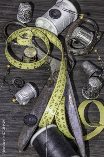 Obraz na płótnie Silver sewing needles, Thimbles, Steel scissors, Measuring tape, Black buttons, Spools of black and white thread including pins on wooden blackground. Sewing items, Sewing notions, Sewing objects. w salonie