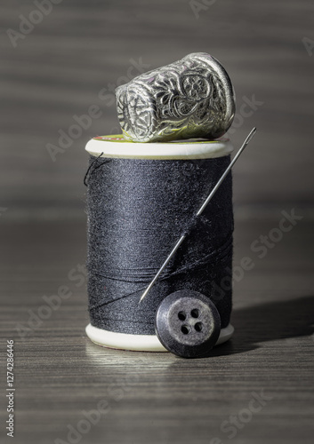 Obraz na płótnie Silver sewing needle stuck in a spool of black thread with Silver thimble on top and black button in front of on wooden table. Sewing items, Sewing notions, Sewing objects, use it as your Wallpaper. w salonie