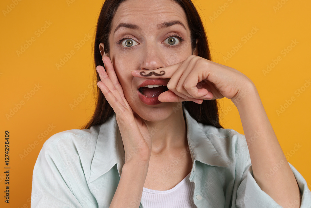 Emotional woman holding finger with drawn mustache above lips on orange background Emotional woman holding finger with drawn mustache above lips on orange background