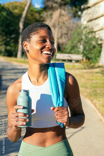Wallpaper Mural Happy black sportswoman smiling and holding water bottle after training in a park Torontodigital.ca