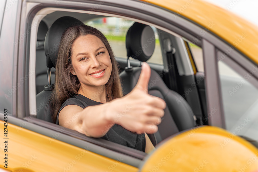 A young woman with long brown hair and a bright smile sits in the driver's seat of a yellow car, giving a thumbs-up gesture through the open window with a confident and positive expression.