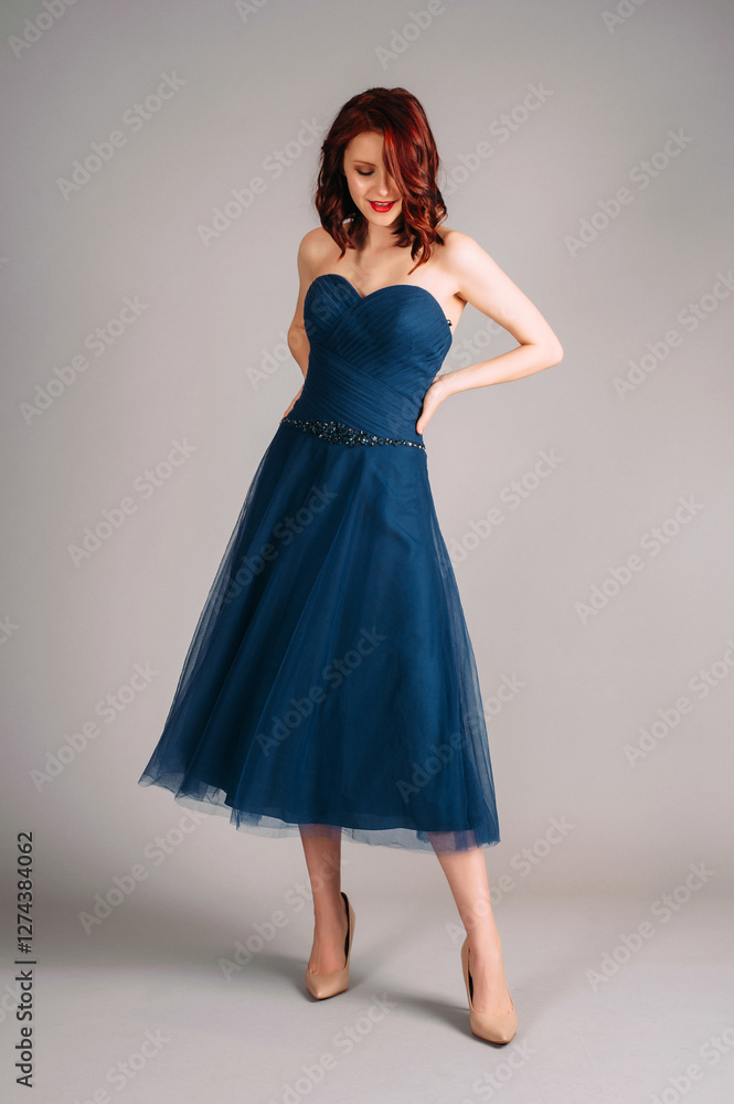 Cheerful redhead woman dancing in studio, smiling portrait. Deep blue sweetheart neckline midi dress. Corset sleeveless classic evening gown, festive outfit. Touching look for an event, flying skirt Cheerful redhead woman dancing in studio, smiling portrait. Deep blue sweetheart neckline midi dress. Corset sleeveless classic evening gown, festive outfit. Touching look for an event, flying skirt