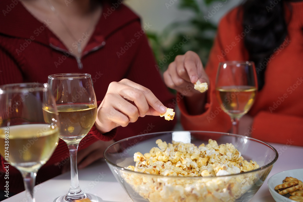 Women enjoying popcorn and white wine during a home party Women enjoying popcorn and white wine during a home party