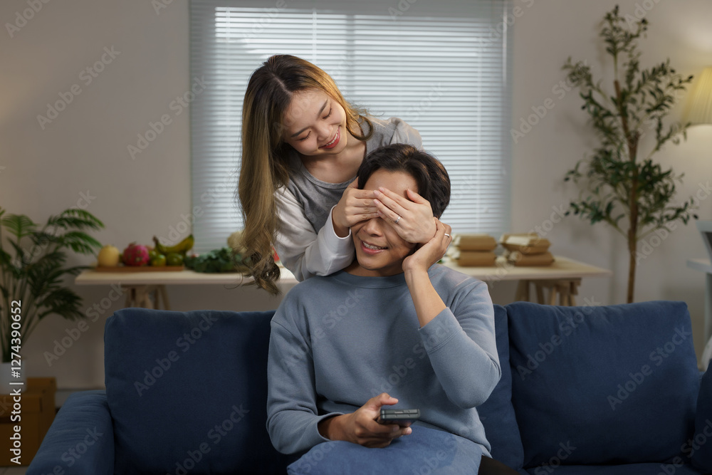Playful woman surprising man covering his eyes on sofa at home Playful woman surprising man covering his eyes on sofa at home