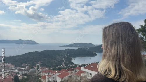 young woman gazes into the distance at a charming European town nestled on a mountainside. The portrait captures the essence of solo travel, digital nomad lifestyle, and the beauty of remote work