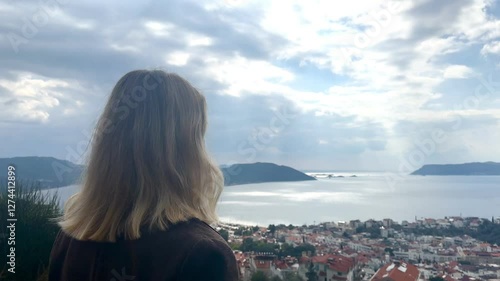 young woman gazes into the distance at a charming European town nestled on a mountainside. The portrait captures the essence of solo travel, digital nomad lifestyle, and the beauty of remote work