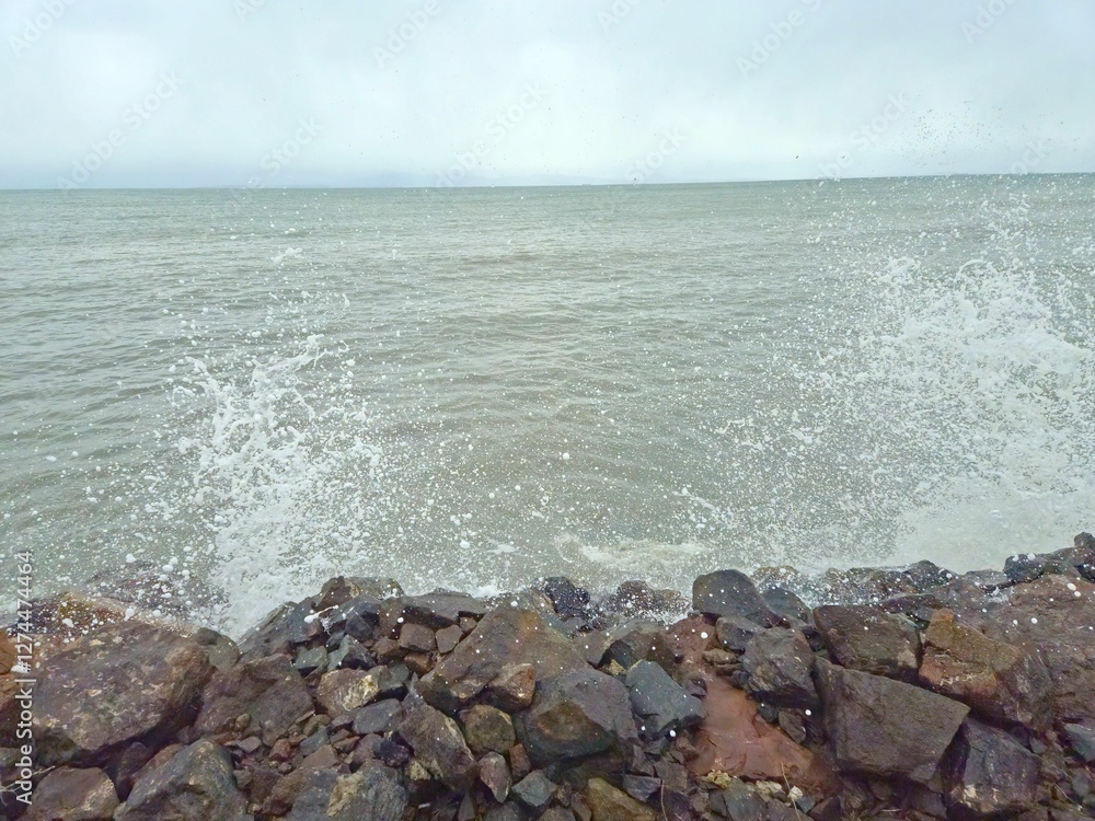 Waves crashing against rocky shore, huge splash in the air, white spray, cloudy sky, greenish water, winter Waves crashing against rocky shore, huge splash in the air, white spray, cloudy sky, greenish water, winter