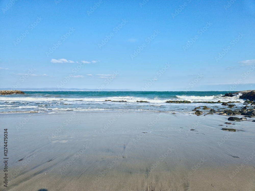 Waves reach the shore on a sunny day at the beach with clear blue skies and gentle winds Waves reach the shore on a sunny day at the beach with clear blue skies and gentle winds