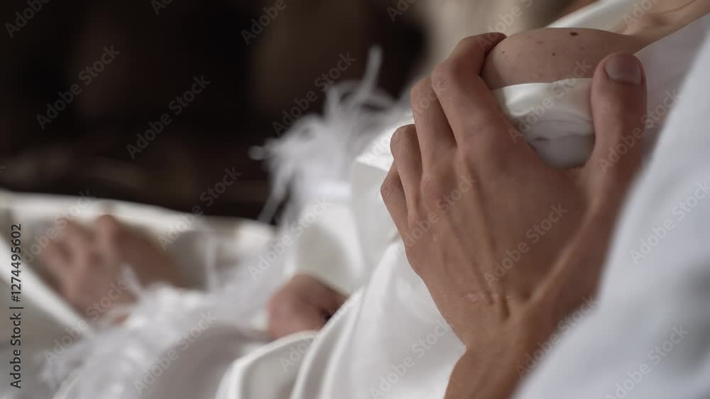 Guy gently strokes young girl's bare shoulder close-up. Morning of the bride and groom in white robe Guy gently strokes young girl's bare shoulder close-up. Morning of the bride and groom in white robe