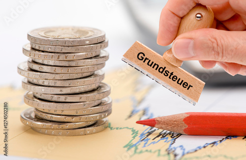 Auf einem finanziellen Diagramm liegt ein Stapel Euromünzen mit Rotstift und ein Stempel mit der Aufschrift Grundsteuer - FOTOMONTAGE photo