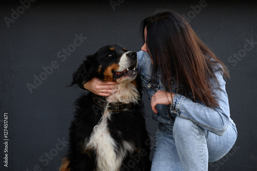 Woman hugging beloved Bernese Mountain Dog while squatting next to him during walk, on black background. Concept of communication with animals, caring for pet, friendship between owner and dog photo