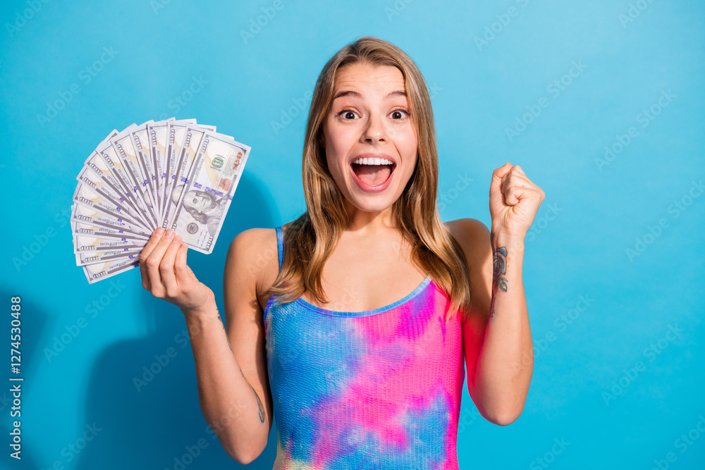 Joyful young woman happily holds dollar bills in a colorful outfit against a vibrant blue background, expressing excitement and success. Joyful young woman happily holds dollar bills in a colorful outfit against a vibrant blue background, expressing excitement and success.