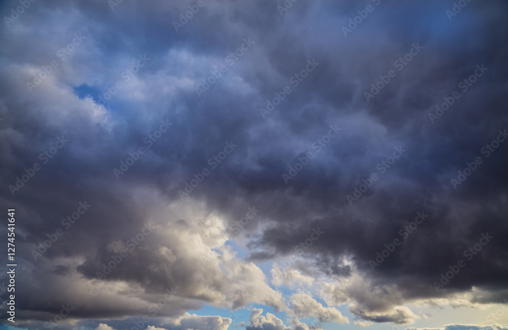 Obraz premium Storm clouds with glimpses of sunlight against the deep blue sky. The dramatic contrast of dark masses and bright rays gives the shot a unique expressiveness.