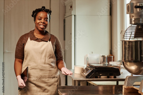 Wallpaper Mural Medium full portrait of young Black female baker wearing apron smiling at camera captured with digital tablet in hands at working station in commercial kitchen Torontodigital.ca