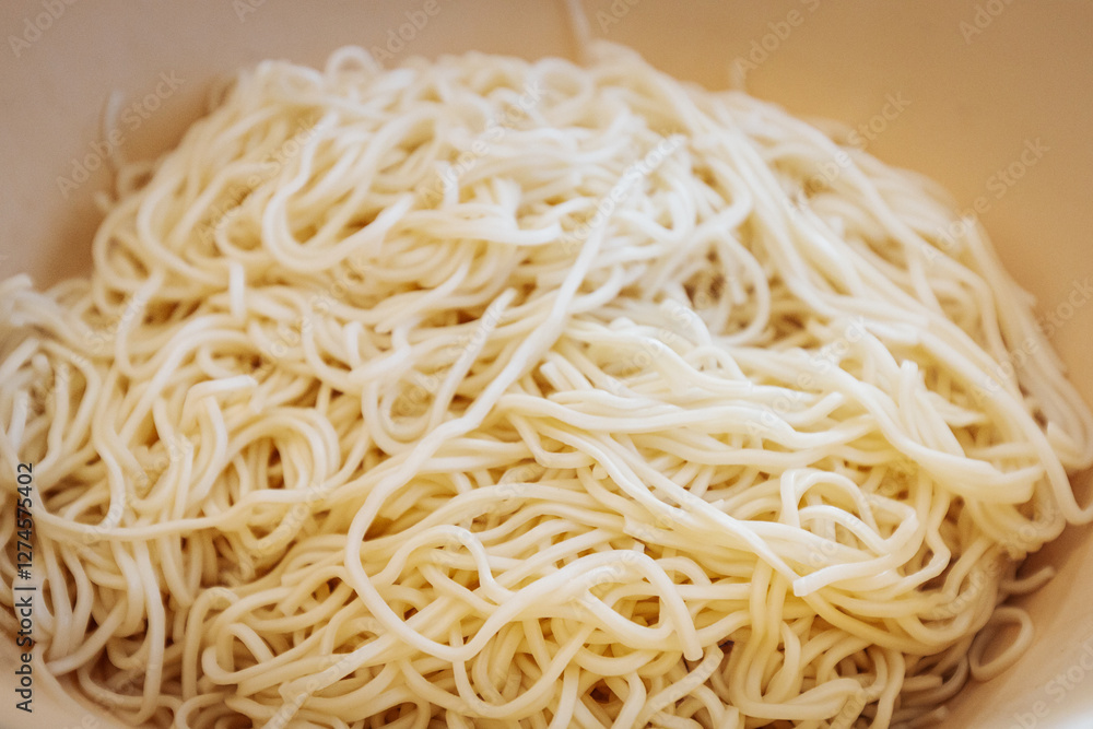 A close-up of freshly cooked noodles in a white bowl. The soft, slightly glossy texture highlights their perfect preparation, ready to be served or mixed with other ingredients.