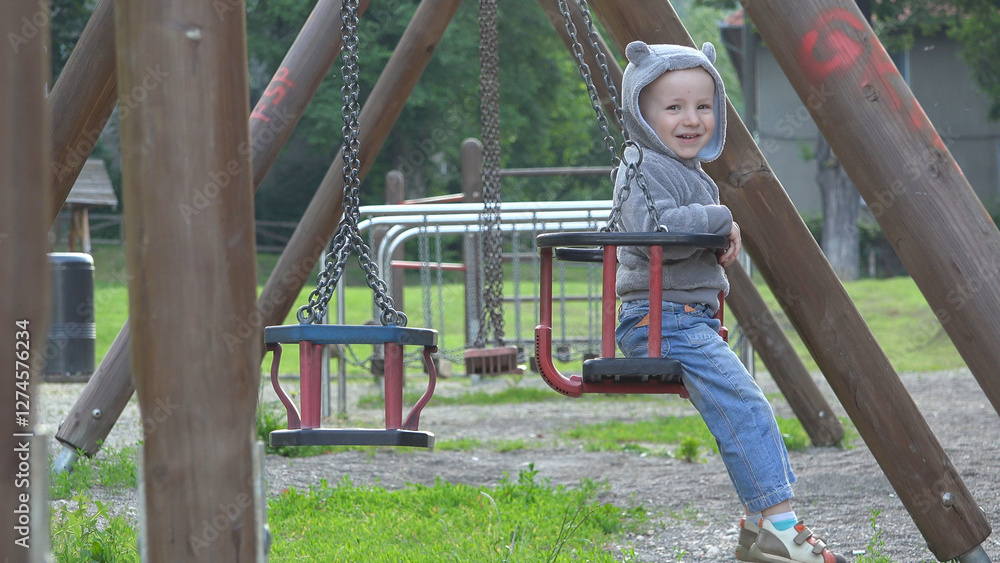 Obraz premium Cheerful kid in swinging chair in park, side view