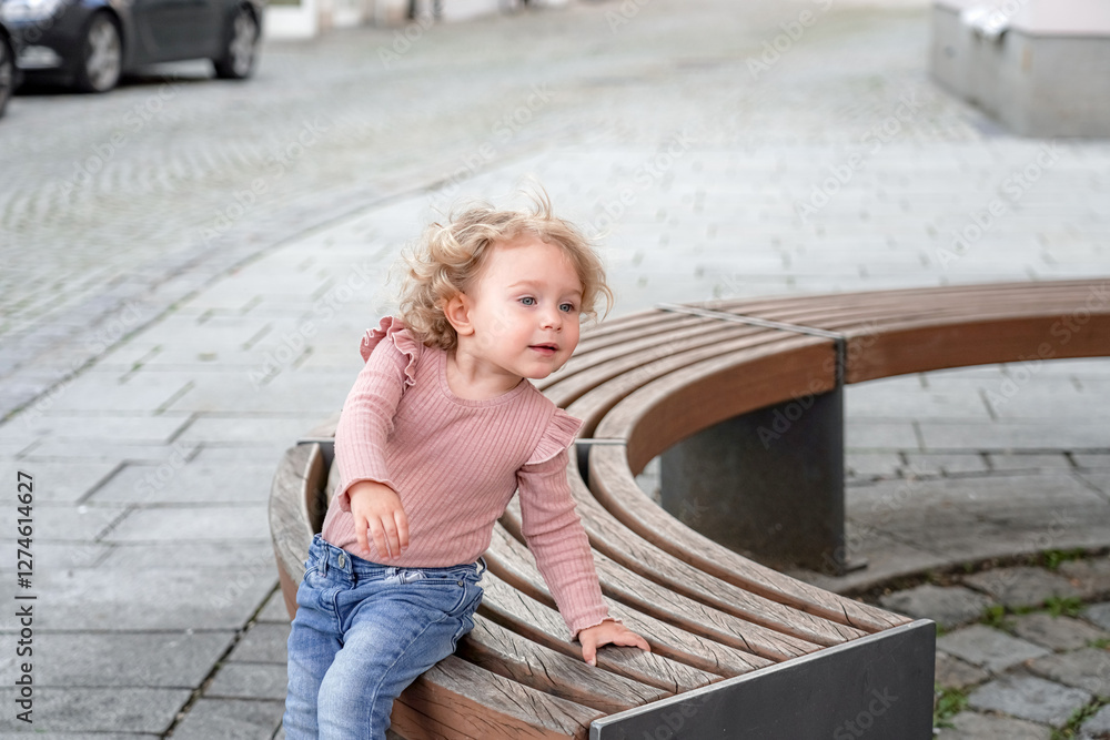 A little girl sits on a bench in the park and looks out. A little girl sits on a bench in the park and looks out.
