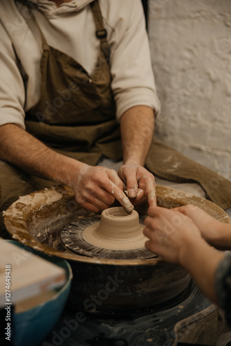 Pottery lesson on a potter's wheel, two people sculpting a shape from clay, hands closeup