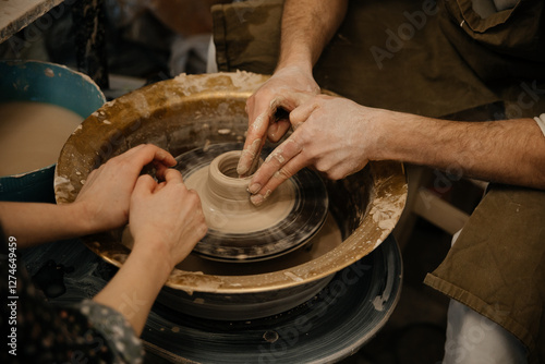 Pottery lesson on a potter's wheel, two people sculpting a shape from clay, hands closeup