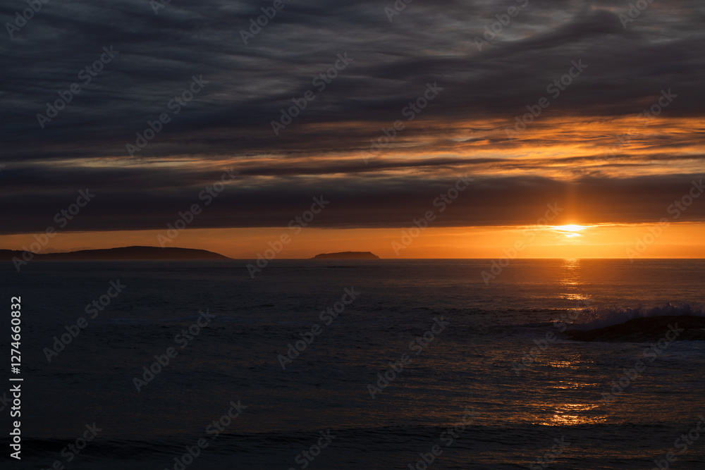 Tranquil sunset over ocean with silhouetted islands and cloudy sky Tranquil sunset over ocean with silhouetted islands and cloudy sky