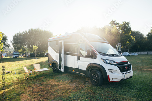 Modern camper van parked in a sunny campground with outdoor chairs