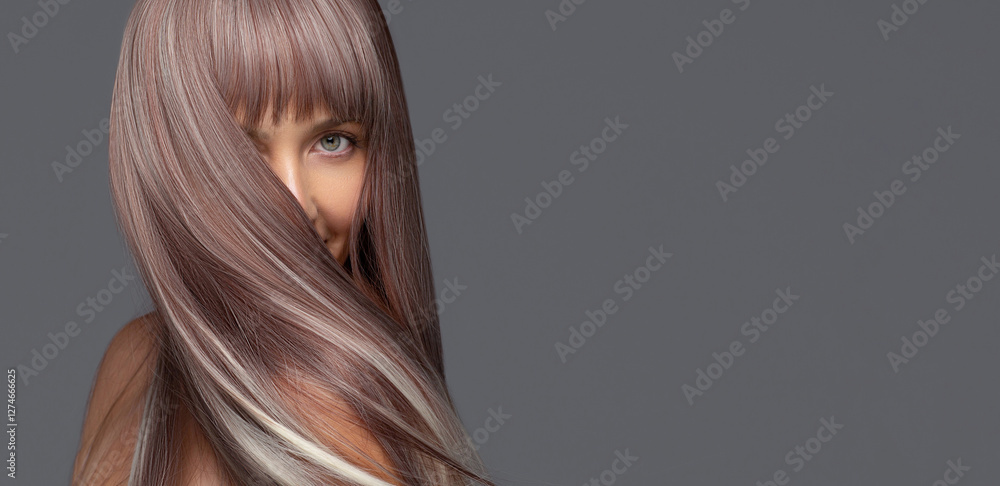 Φωτογραφία Woman with long, silky, ash brown flying hair with platinum highlights covering part of her face, looking at the camera with a soft expression against a gray background