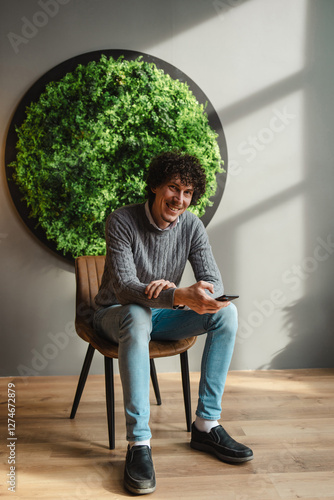 Young man with curly hair sitting by green wall symbolizing sustainable living