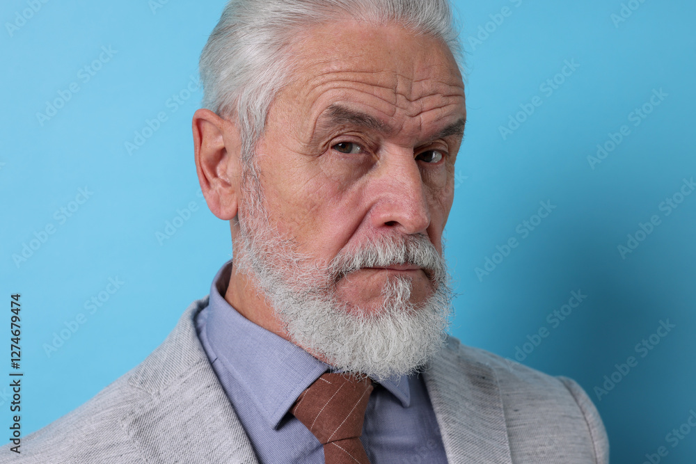 Portrait of serious senior man with silver beard on light blue background Portrait of serious senior man with silver beard on light blue background