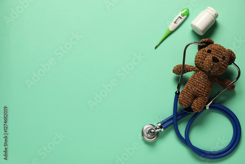 Pediatrics concept. Toy bear with stethoscope, pills and thermometer on turquoise background, flat lay. Space for text photo