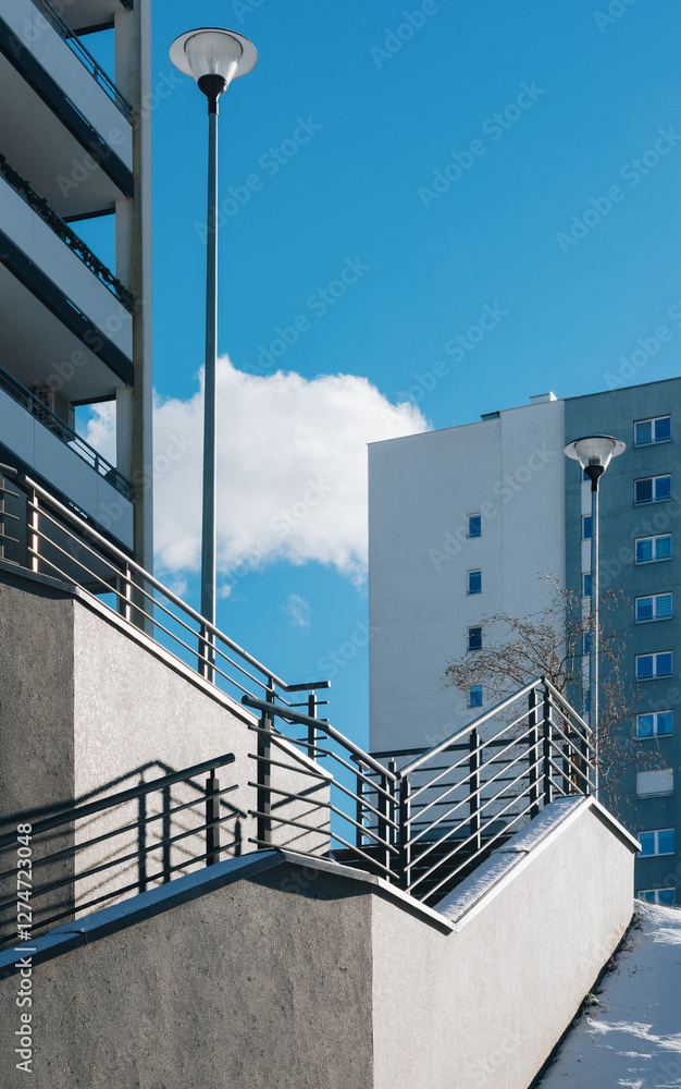 Fototapeta premium Modern Urban Staircase with Railings, Residential Buildings, and Lamp Post Under a Blue Sky