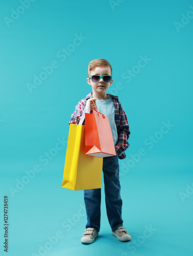 Cute little boy with shopping bags on light blue background