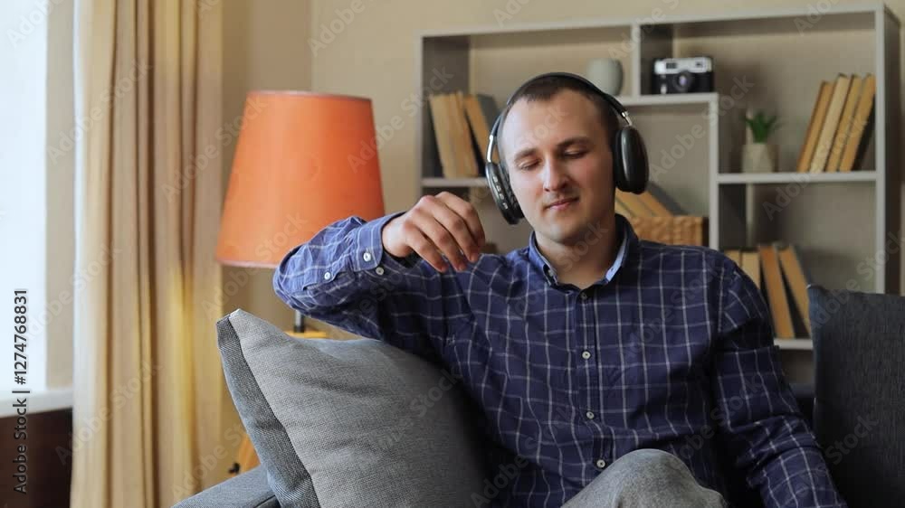 Relaxed young man wearing wireless headphones, dancing and enjoying music on smartphone while sitting comfortably on living room sofa, embodying carefree leisure moment
Relaxed young man wearing wireless headphones, dancing and enjoying music on smartphone while sitting comfortably on living room sofa, embodying carefree leisure moment