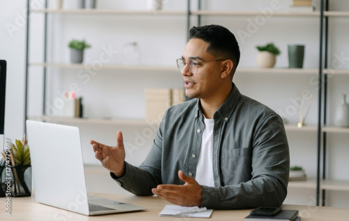 A man wearing glasses is sitting at a desk with a laptop in front of him