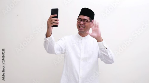 Muslim man answering a video call and waving his hand to greet 