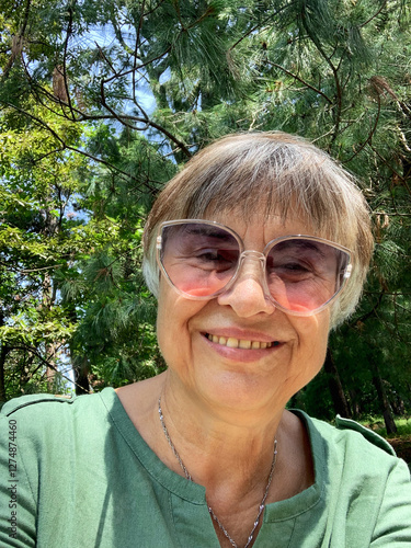 Fotografie Caucasian senior woman in a green dress takes a selfie portrait while sitting on