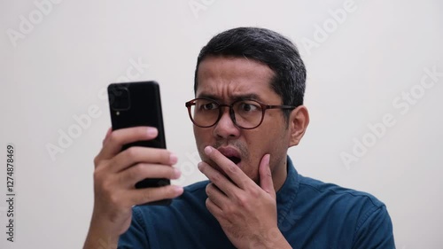 Close up shot of a man showing confused face when looking at his phone