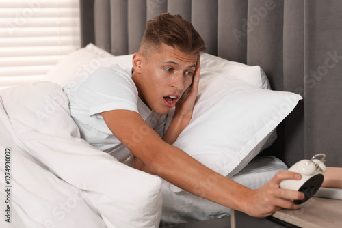 Overslept man with alarm clock in bed at home photo