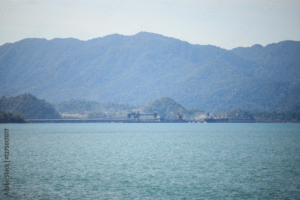 Distance view of cement quarry with mountainous background. Gravel conveyor machine. Gravel transportation ship by the harbour. Mining industry. Distance view of cement quarry with mountainous background. Gravel conveyor machine. Gravel transportation ship by the harbour. Mining industry.