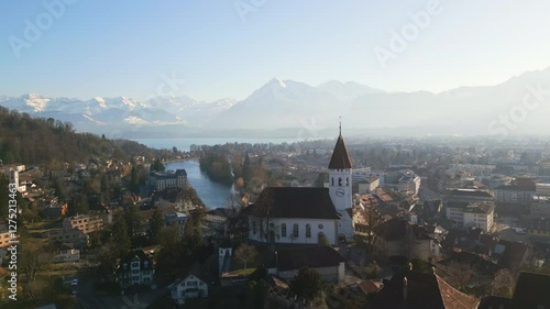 Wallpaper Mural A stunning aerial view of a medieval church in the historic old town of Thun, Switzerland, surrounded by charming rooftops, a scenic river, and majestic mountains Torontodigital.ca