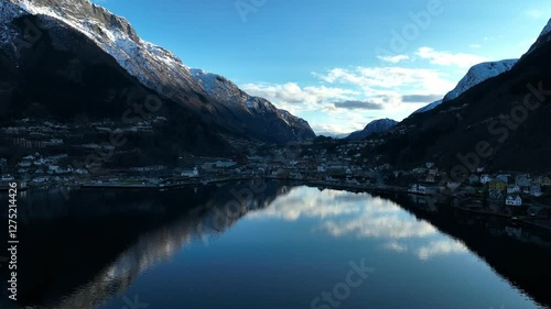 Snow capped peaks and glossy fjord in Odda Norway in clear winter evening. Valley in shadow, bright sky above photo