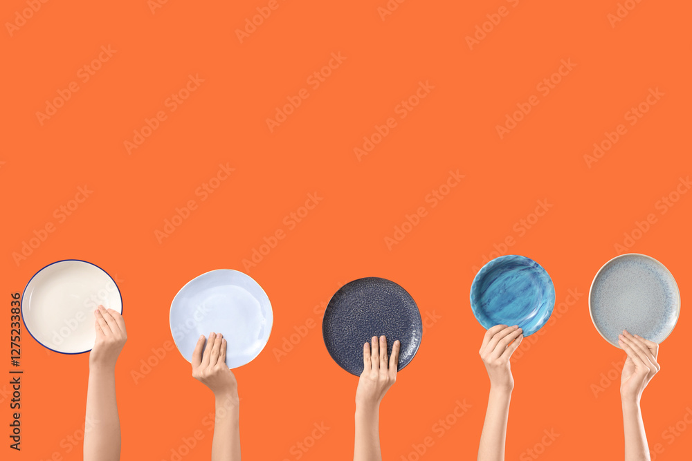 Female hands with different plates on orange background Female hands with different plates on orange background