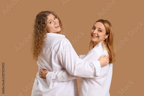 Beautiful women in white shirts hugging on brown background, back view. Women's History Month