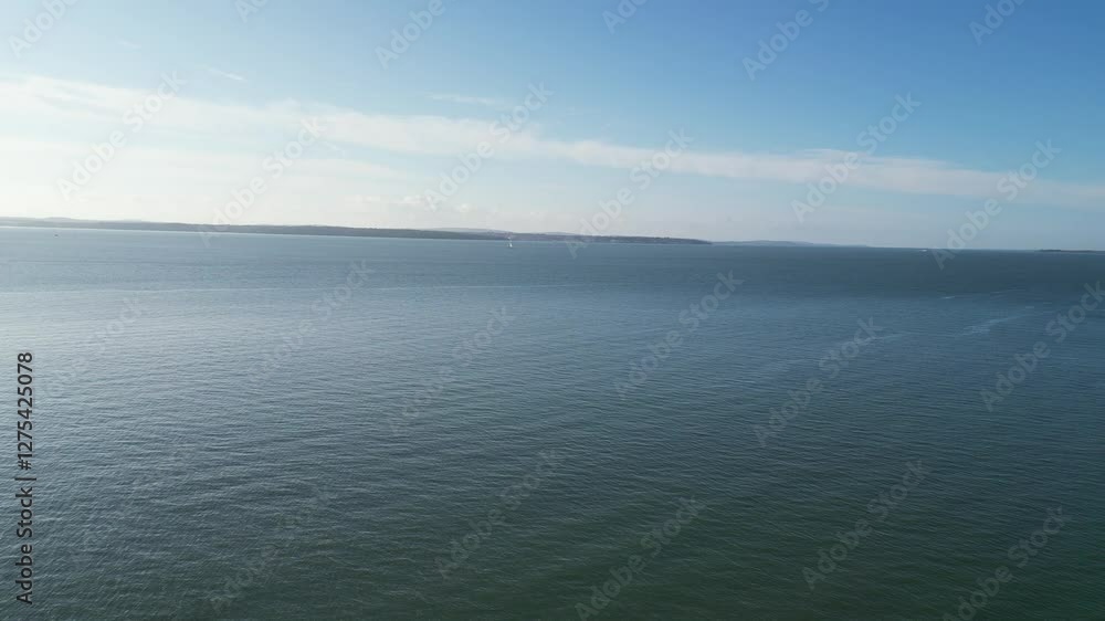 A vast, calm ocean stretches to the horizon under a clear blue sky, with gentle ripples on the water's surface and a faint distant shoreline in the background. A vast, calm ocean stretches to the horizon under a clear blue sky, with gentle ripples on the water's surface and a faint distant shoreline in the background.