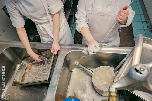 Chefs scrubbing and cleaning dishes in a busy professional kitchen. Hygiene, teamwork, and kitchen maintenance are essential in the food industry.